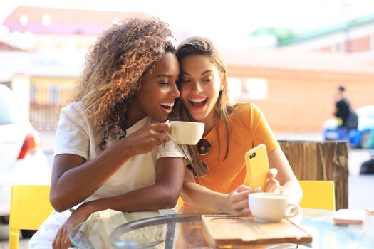 Two beautiful young woman sitting at cafe drinking coffee and looking at mobile phone