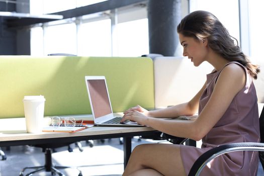 Beautiful business woman in smart casual wear working on laptop in the office.