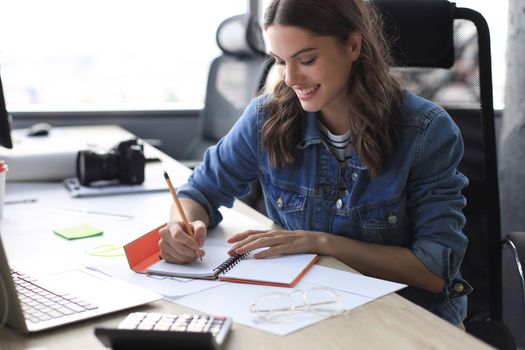 Happy young woman writing something down while working in the office
