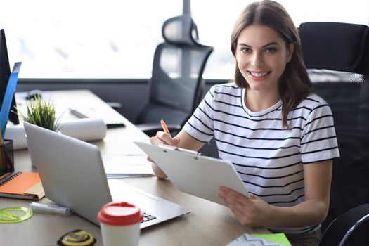 Beautiful young woman is sitting in the office and looking at camera