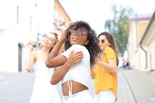 Three young smiling hipster women in summer clothes posing on street.Female showing positive face emotions