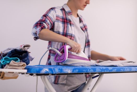 beautiful young red haired housewife in good mood ironing clothes on ironing board in front of a white wall at home