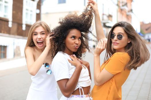 Three young smiling hipster women in summer clothes posing on street.Female showing positive face emotions