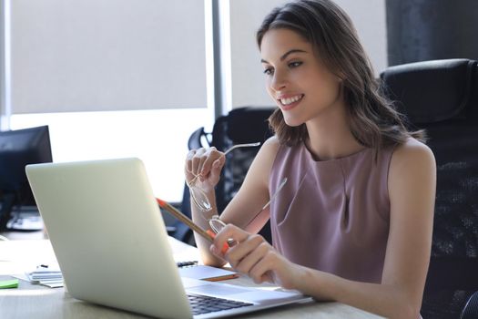 Beautiful business woman in smart casual wear working on laptop in the office.