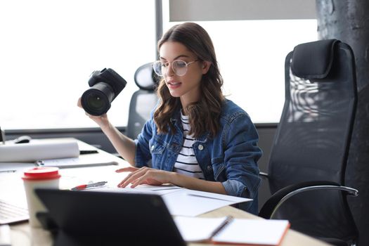 Young architect holding digital camera and looking on blueprint while working in the creative office