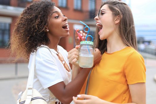 Trendy cool hipster girls, friends drink cocktail in urban city background