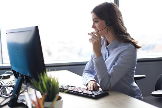 Beautiful smiling call center worker in headphones is working at modern office.
