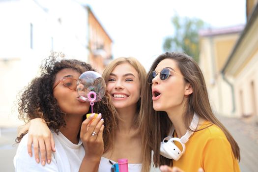 Three happy beautiful women blowing soap bubbles in city street