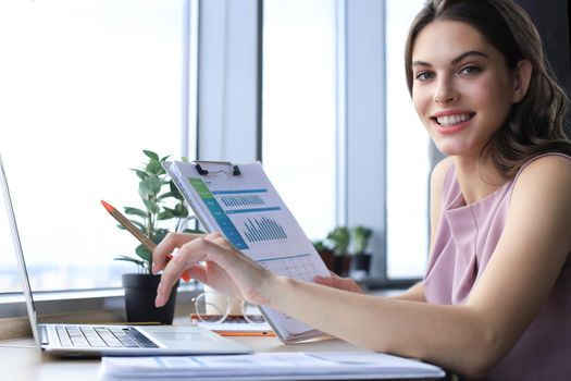Beautiful young woman writing something down while sitting in modern office