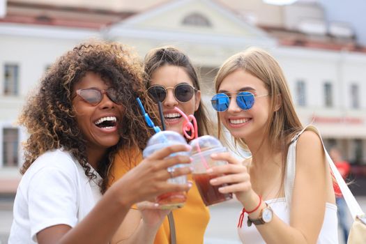 Three trendy cool hipster girls, friends drink cocktail in urban city background
