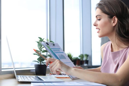 Beautiful young woman using laptop and looking at it while sitting at her working place