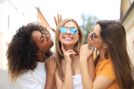 Three young smiling hipster women in summer clothes posing on street.Female showing positive face emotions