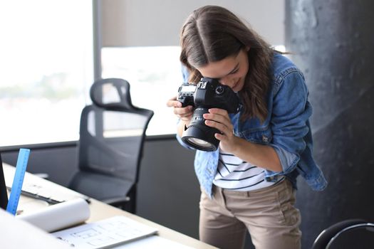 Concentrated young designer using digital camera while standing near the desk in her creative office