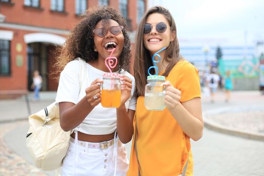 Trendy cool hipster girls, friends drink cocktail in urban city background