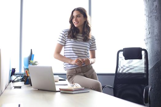 Attractive young woman looking away while sitting on the desk in office