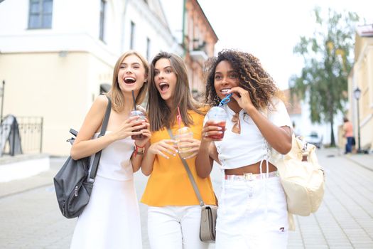 Three trendy cool hipster girls, friends drink cocktail in urban city background