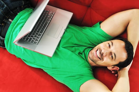 young man relax on red sofa and work on laptop at home indoor