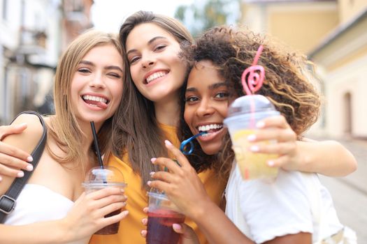 Three trendy cool hipster girls, friends drink cocktail in urban city background