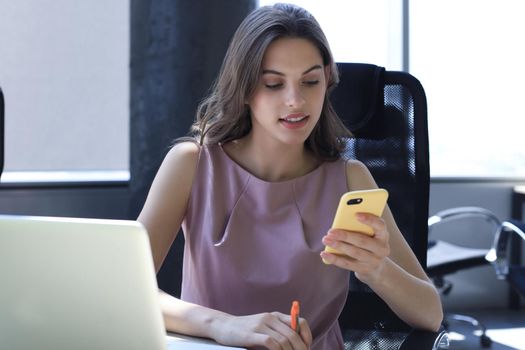 Attractive business woman using smart phone while sitting at the office desk