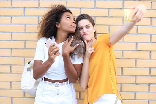 Two young smiling hipster women in summer clothes posing on street.Female showing positive face emotions