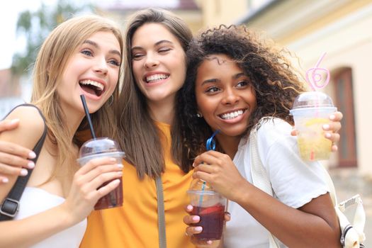 Three trendy cool hipster girls, friends drink cocktail in urban city background