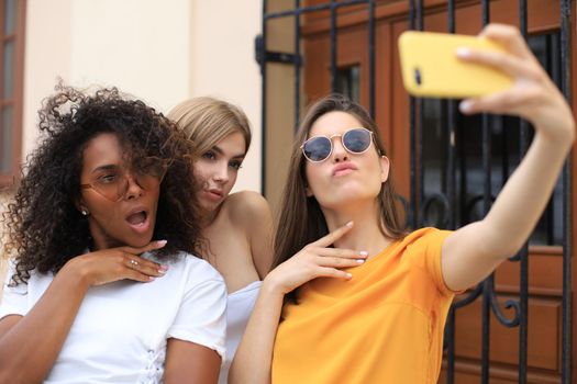 Three cute young girls friends having fun together, taking a selfie at the city