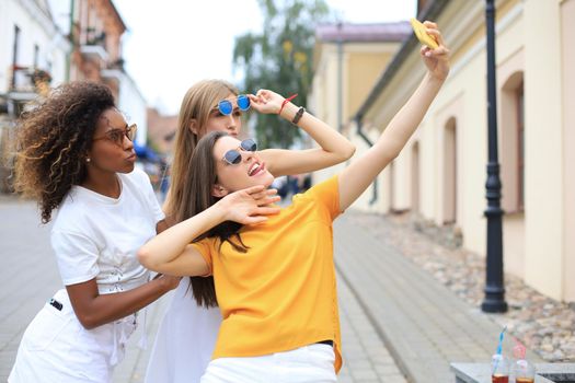 Three cute young girls friends having fun together, taking a selfie at the city