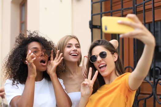 Three cute young girls friends having fun together, taking a selfie at the city