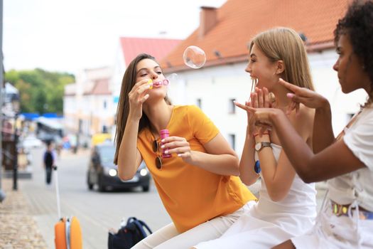 Three happy beautiful women blowing soap bubbles in city street