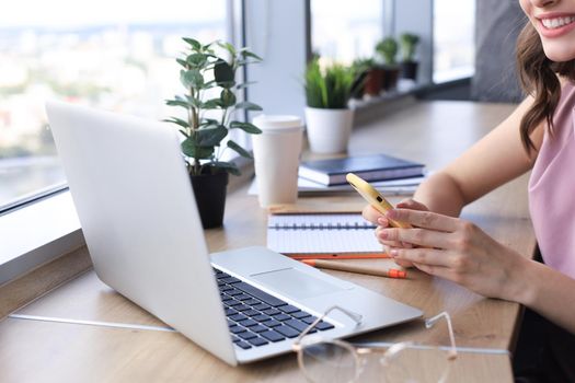 Close-up of businesswoman hands using smart phone while working on laptop