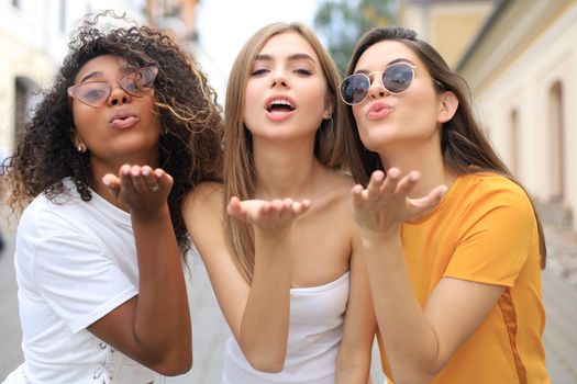 Three young smiling hipster women in summer clothes posing on street.Female showing positive face emotions