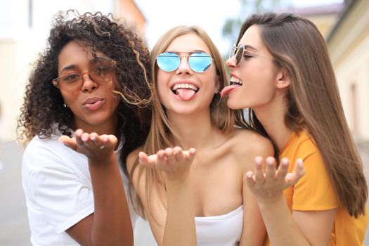 Three young smiling hipster women in summer clothes posing on street.Female showing positive face emotions