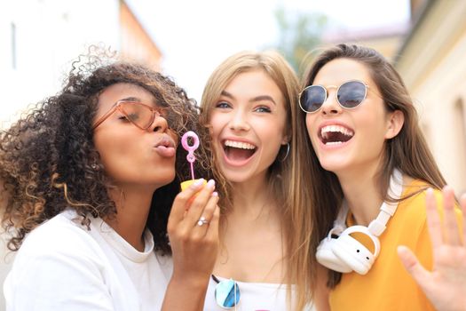 Three happy beautiful women blowing soap bubbles in city street