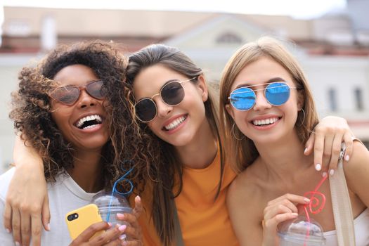 Three trendy cool hipster girls, friends drink cocktail in urban city background