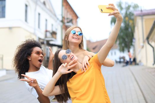 Three cute young girls friends having fun together, taking a selfie at the city