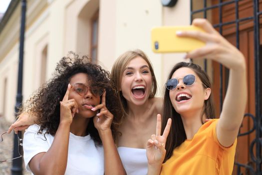 Three cute young girls friends having fun together, taking a selfie at the city
