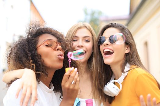 Three happy beautiful women blowing soap bubbles in city street