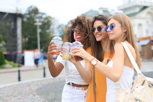 Three trendy cool hipster girls, friends drink cocktail in urban city background