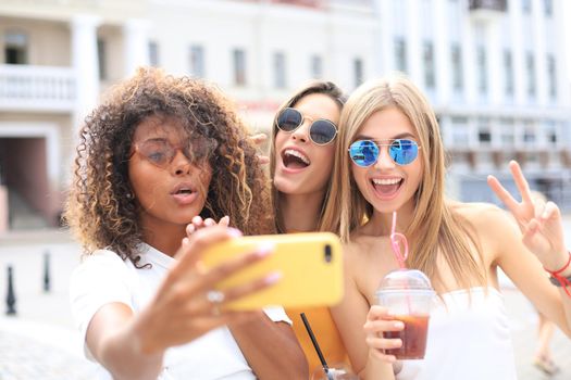 Three cute young girls friends having fun together, taking a selfie at the city