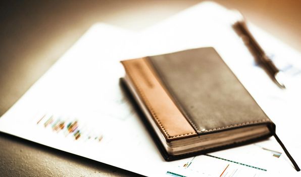 personal organizer and pen on the desk on the background of graphs and charts to your phone