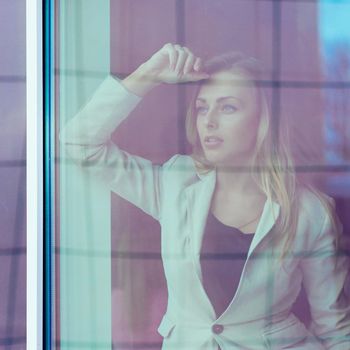 photo from behind the glass: successful woman leader looks out the window of his personal office