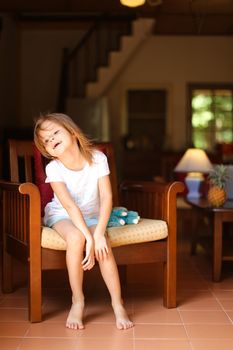 Little happy female kid sitting with toy in wooden chair. Concept of kid model and wood in interior.