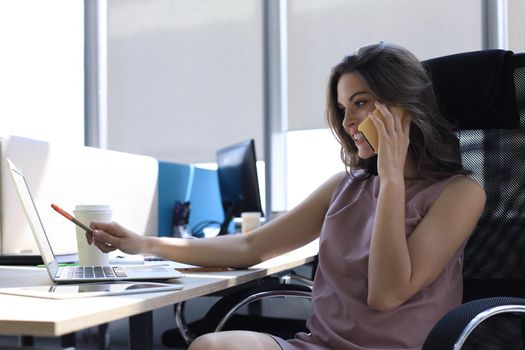 Attractive business woman talking with collegues on the mobile phone while sitting in the office desk.