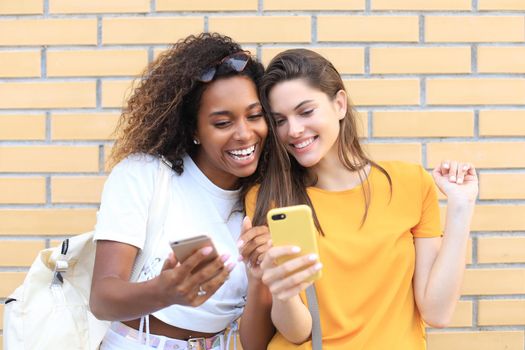 Two young smiling hipster women in summer clothes posing on street.Female showing positive face emotions