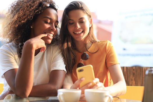 Two beautiful young woman sitting at cafe drinking coffee and looking at mobile phone