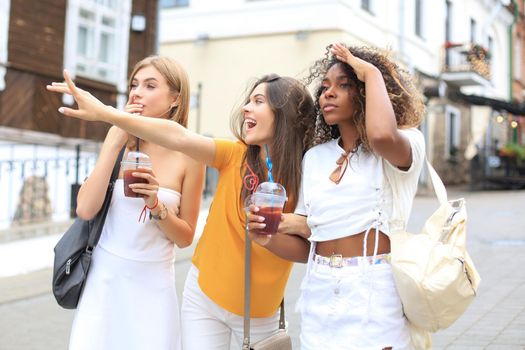 Three trendy cool hipster girls, friends drink cocktail in urban city background