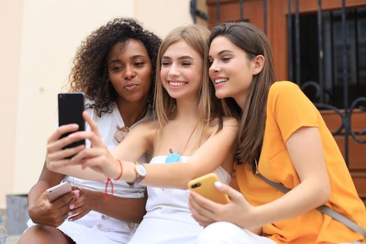 Three cute young girls friends having fun together, taking a selfie at the city