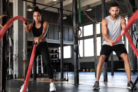 Athletic young couple with battle rope doing exercise in functional training fitness gym