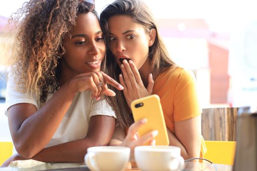 Two beautiful young woman sitting at cafe drinking coffee and looking at mobile phone