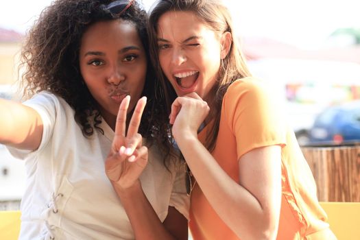 Cute young girls friends having fun together, taking a selfie while sitting at cafe